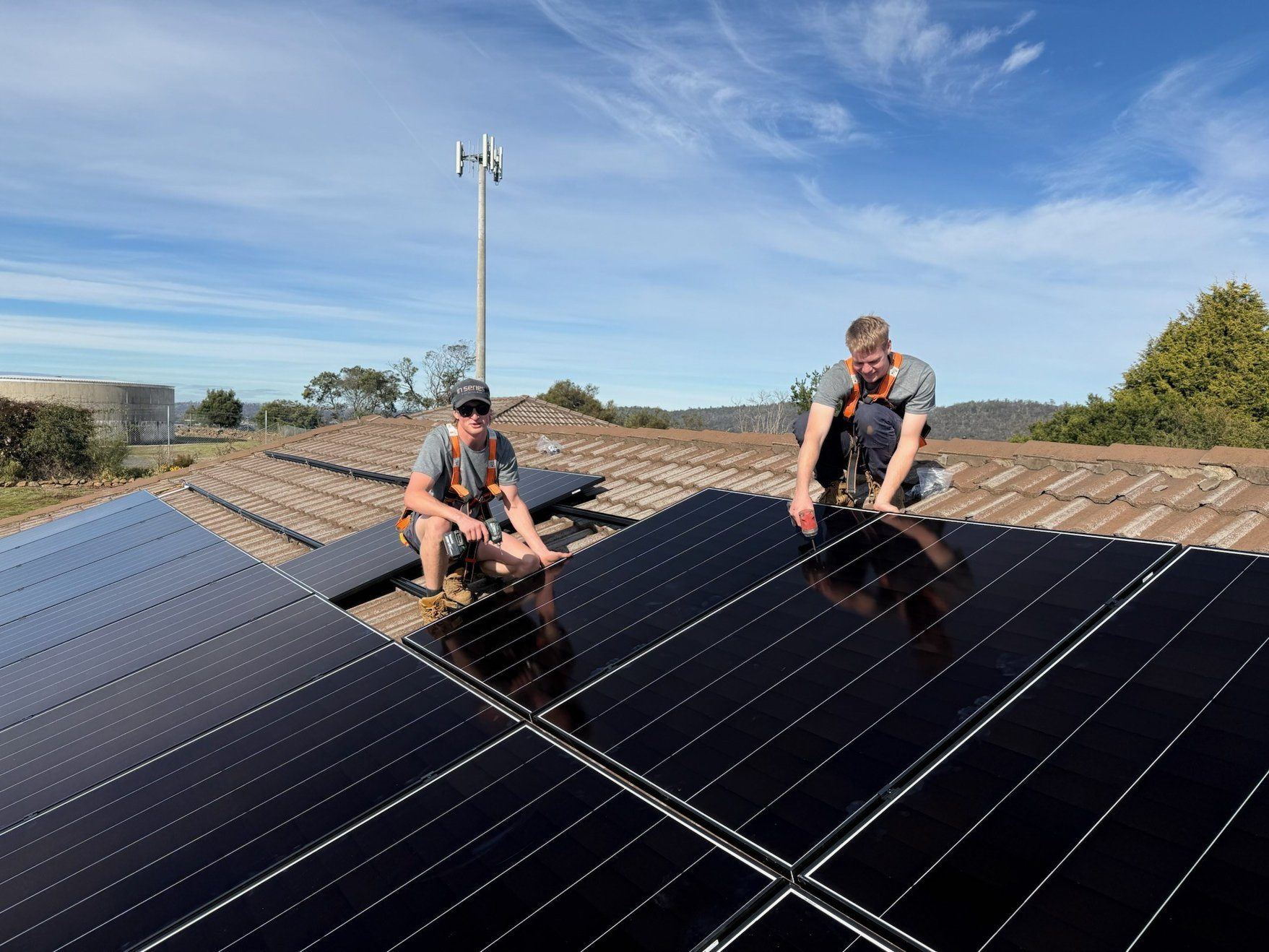 Two In Series installers fitting solar panels on a Tasmanian rooftop on a clear day