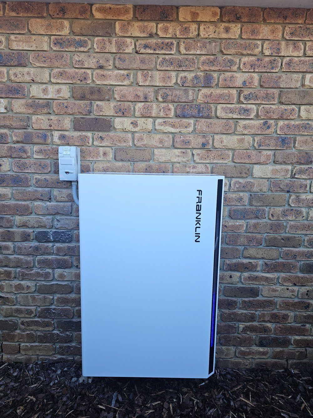FranklinWH aPower battery unit installed against a brick exterior wall