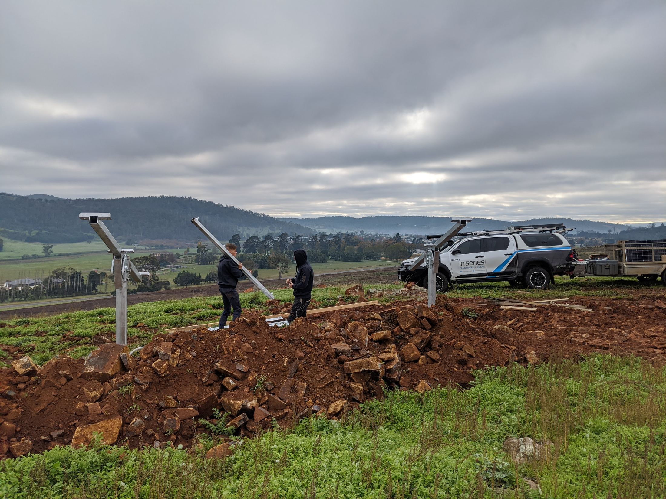 Two In Series installers setting up solar mounting rails on a hilltop, with the branded In Series ute behind them
